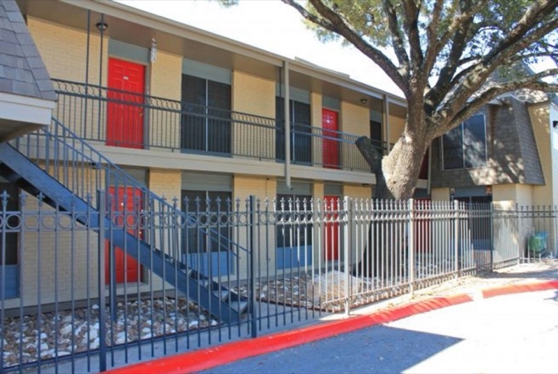 The Hamilton Place courtyard elevation: two stories of buff brick, red doors and a live oak over the walk.